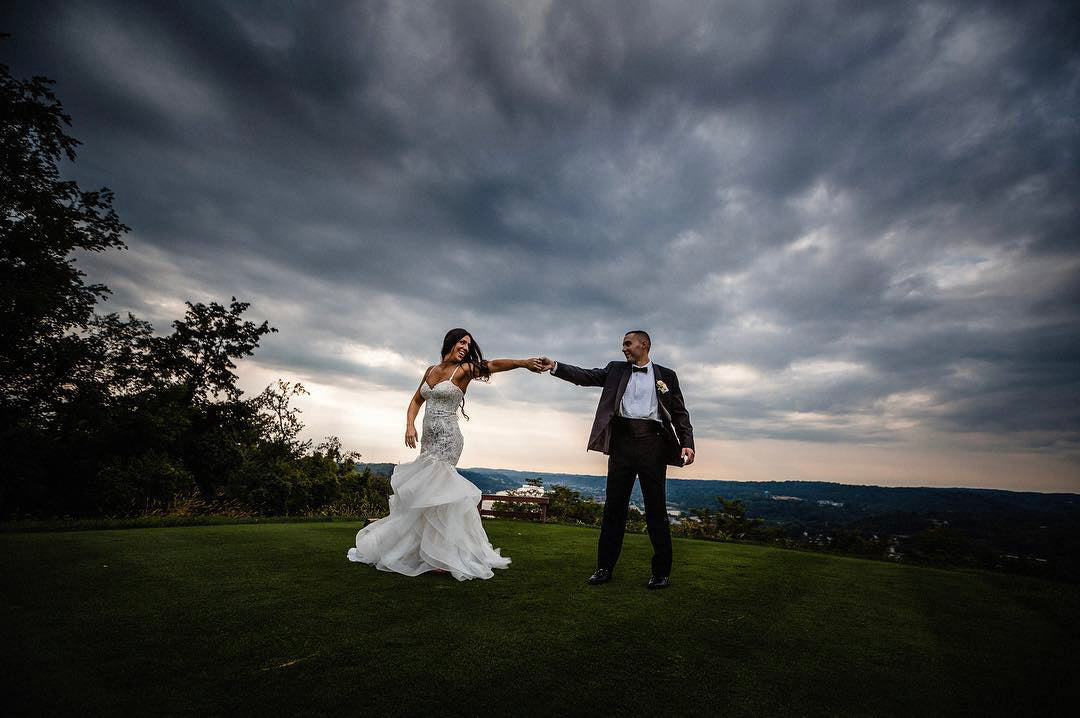 a wedding couple dancing outside in their wedding dress while it is heavily cloudy 