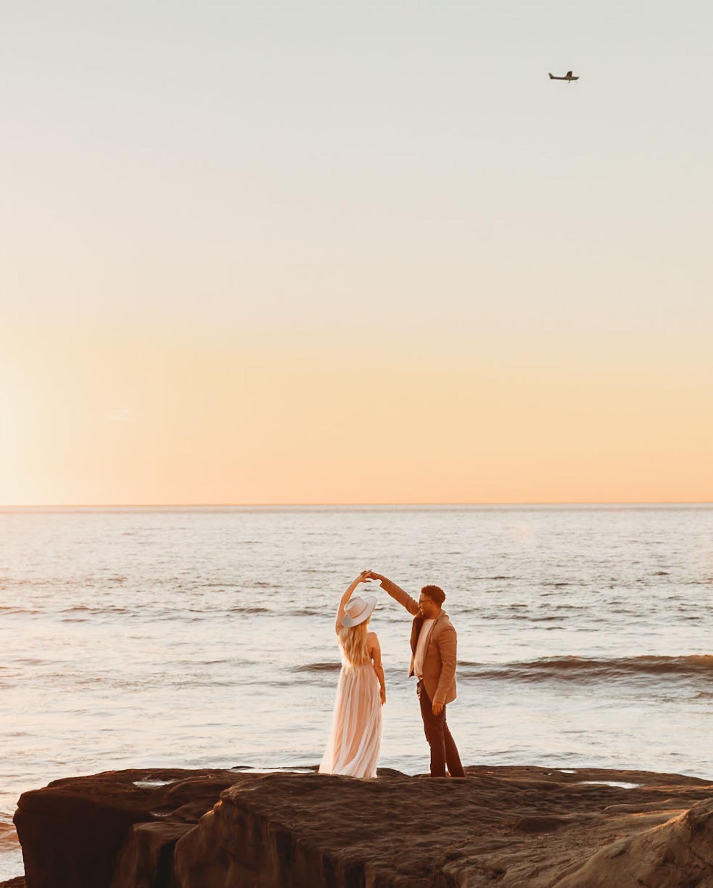 a groom twirling the bride to be by her hand on the sea beach