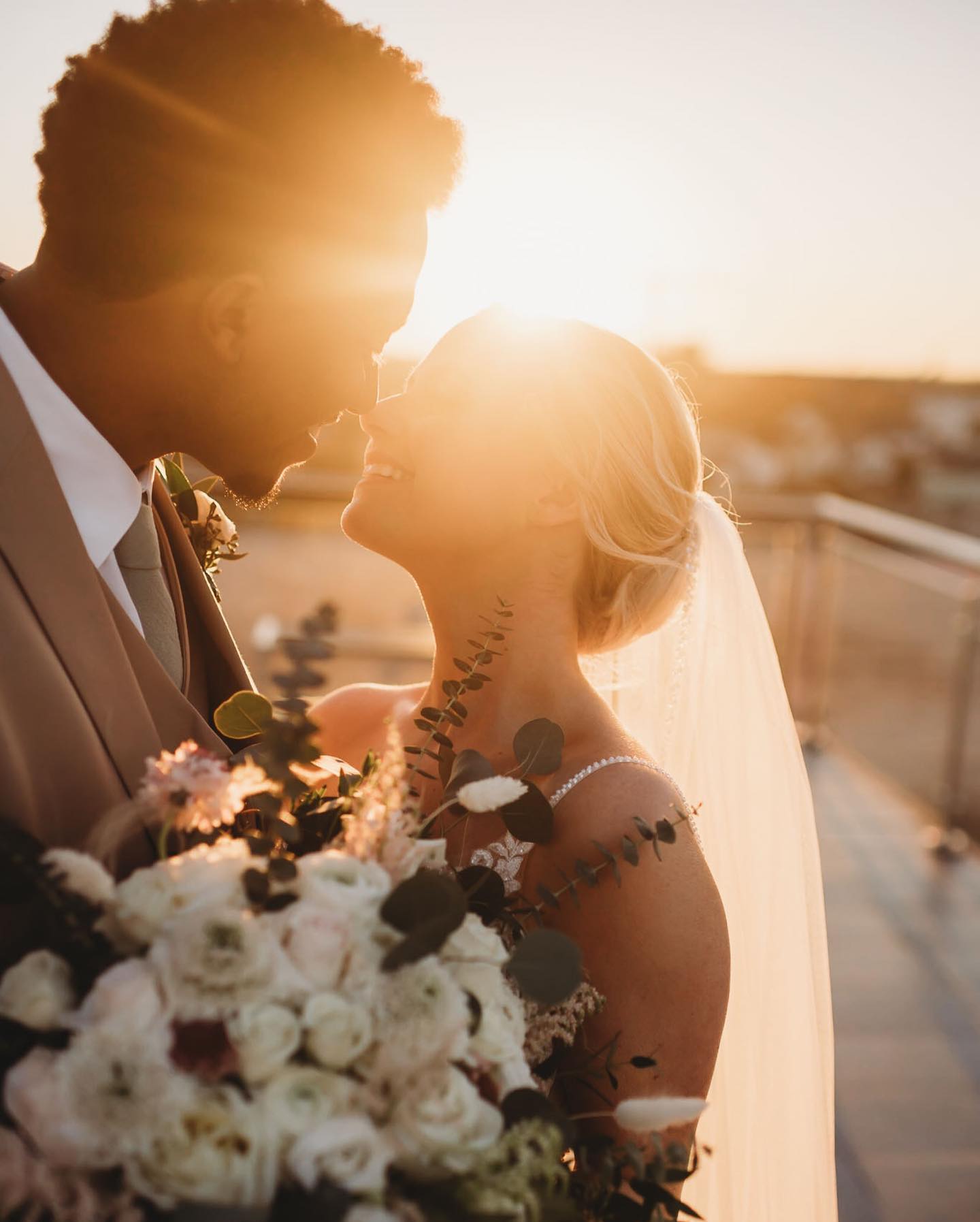a wedding couple looking at each other holding their wedding bouquet during the sunset