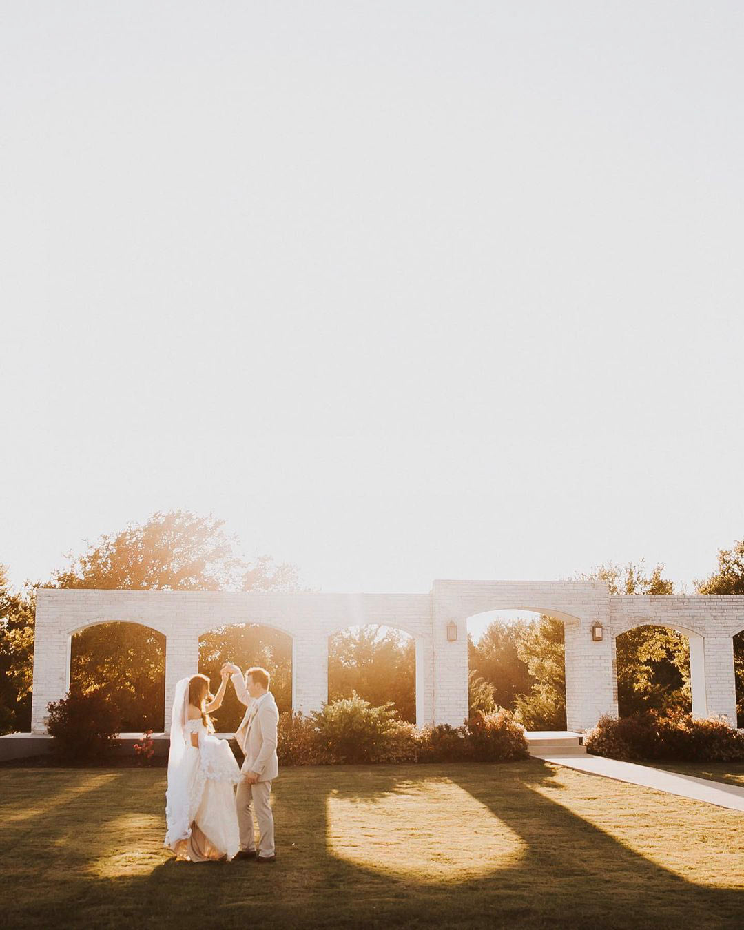 a wedding couple posing standing on the lawn with bright sunlight in the background