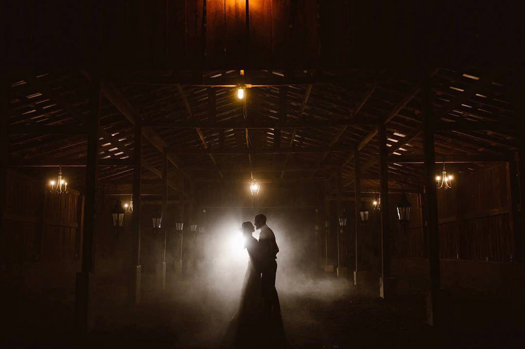 a silhouette of couple posing holding each other in a barn