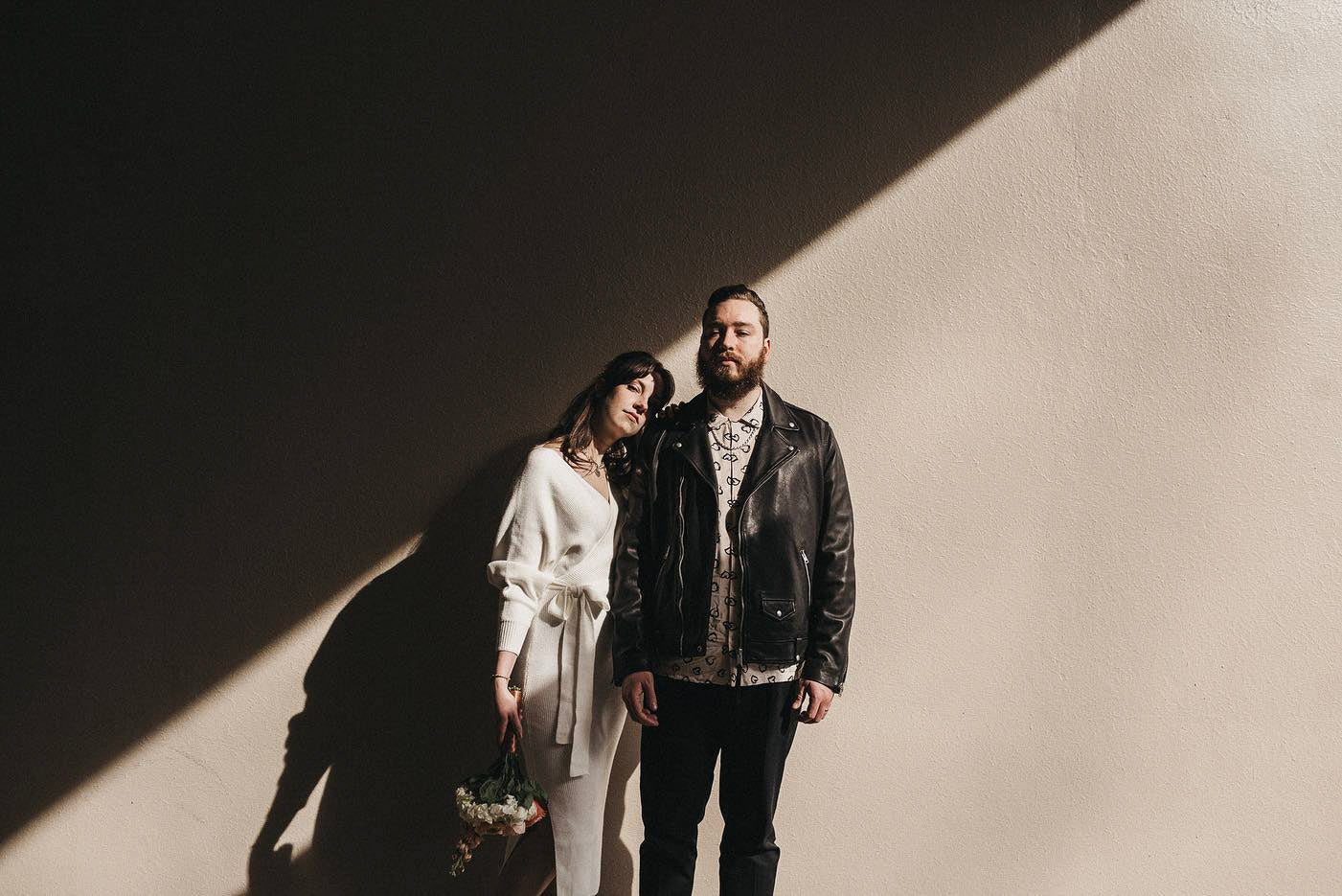 a couple posing standing against a wall while a diagonal shadow falls on them