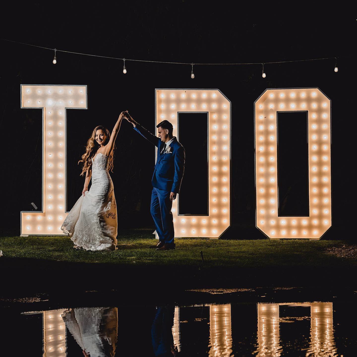 a wedding couple dancing in front of a giant i do sign