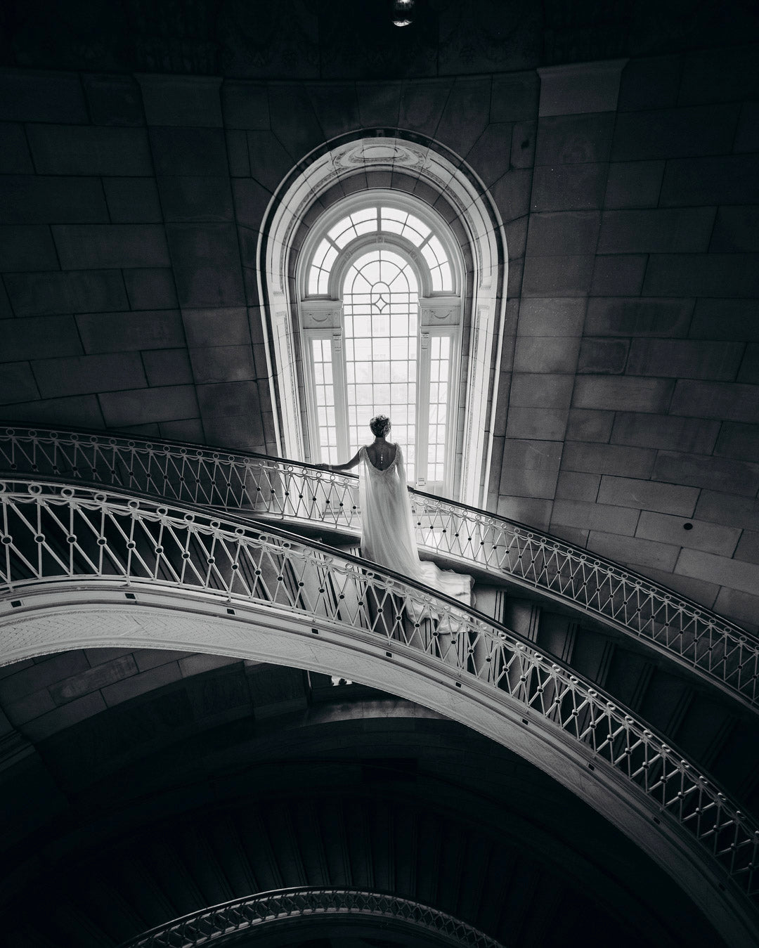 a wedding bride looking outside the window from a large rounded staircase