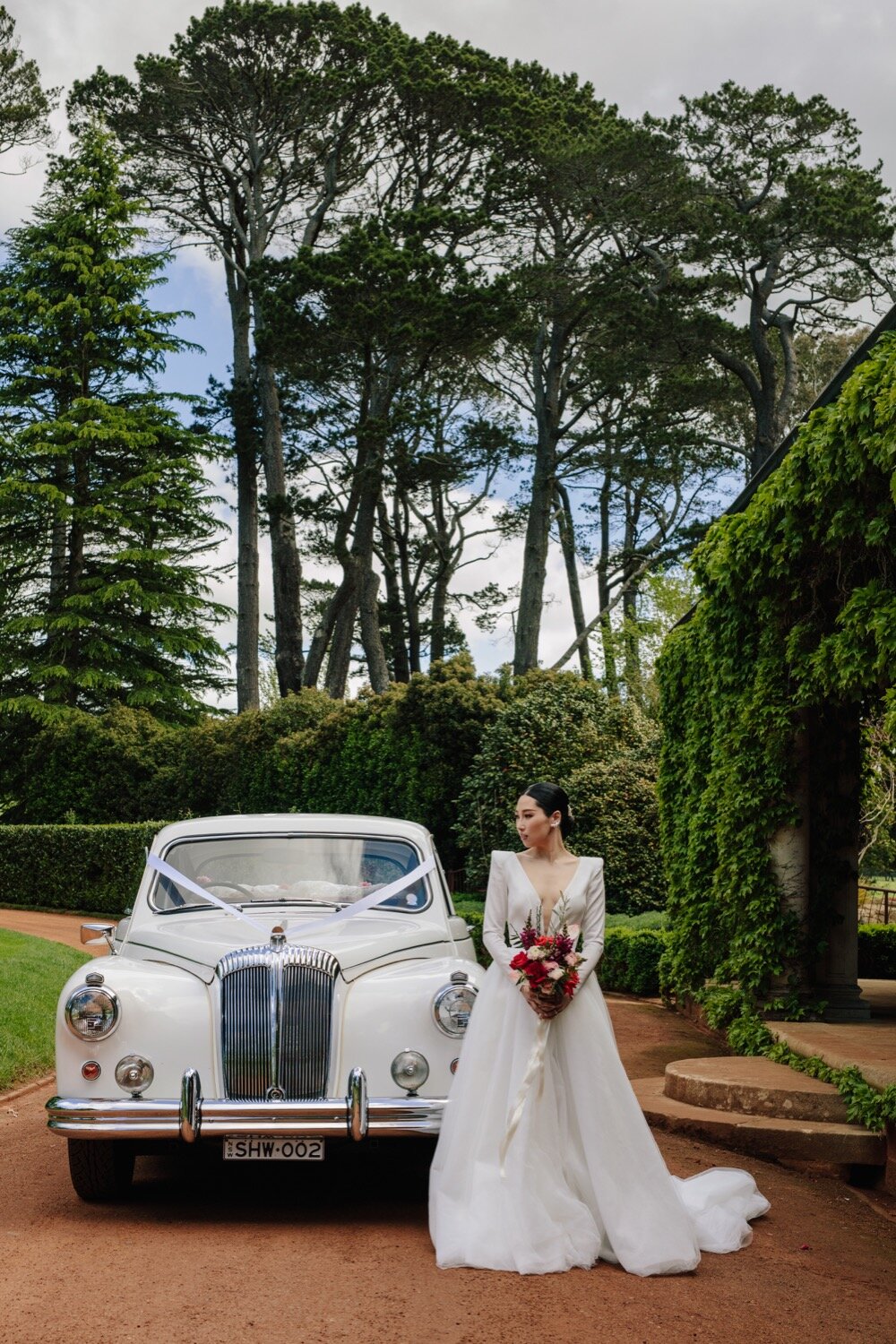 bride posing with car at bendooley book barn photography hilary cam