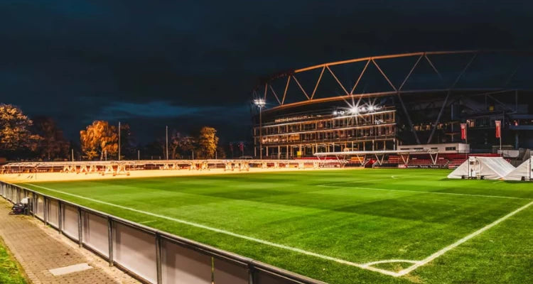 Soccer stadium at night with illuminated stands and green field.