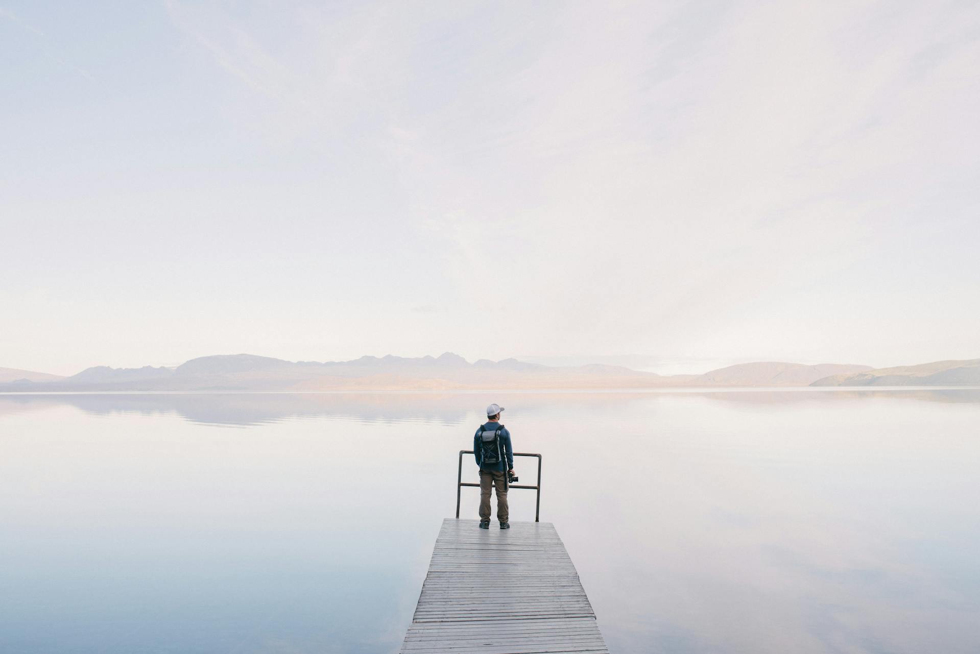 Man Wearing Jacket Standing on Wooden Docks Leading to Body of Water by Wouter de Jong