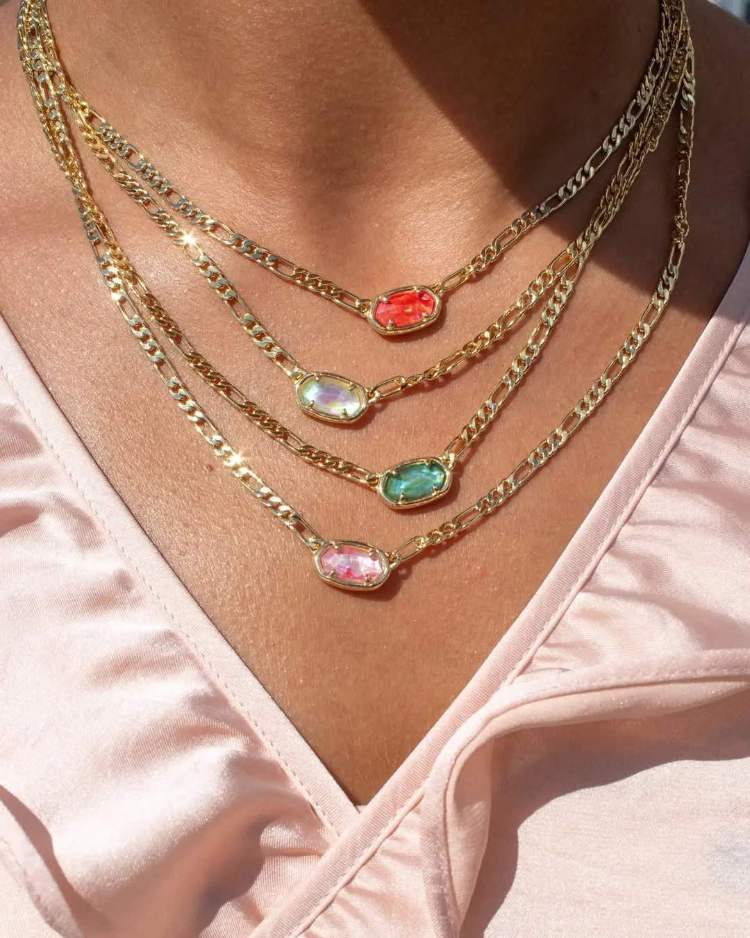 Woman in a pink satin top wears four layered gold-tone chain necklaces with oval gemstones in red, iridescent, green, and pink.