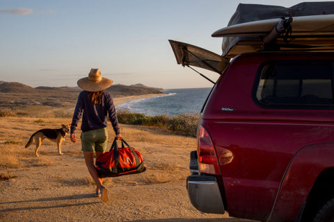 A woman and dog on a beach with a duffel bag