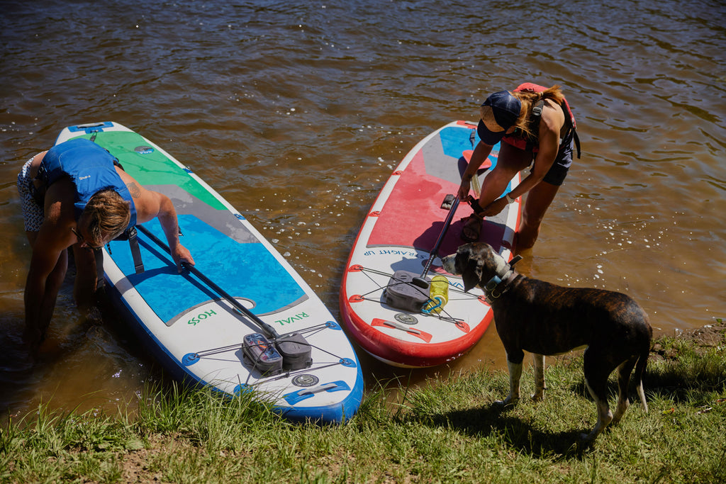 A dog and two women get ready to stand-up paddleboard