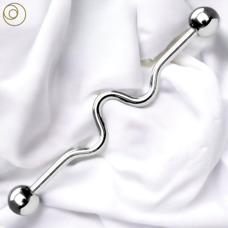 A 14g wavy industrial barbell in surgical steel pictured diagonally against a white fabric background.