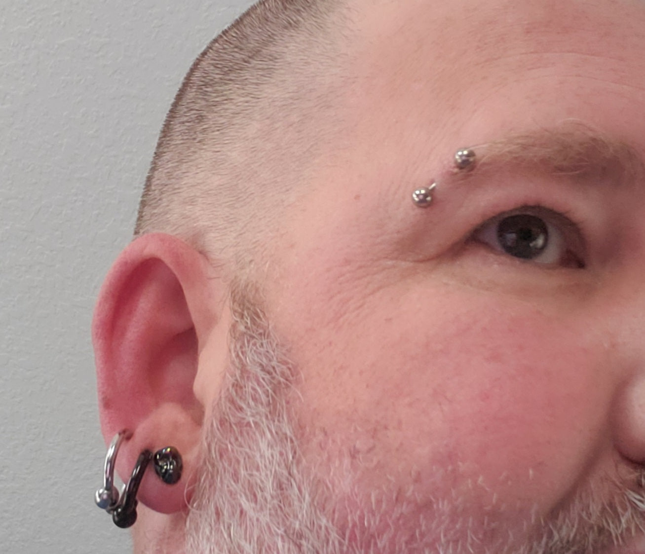 A horizontal eyebrow piercing on the face of a man that has a curved barbell through it along with three earlobe piercings.