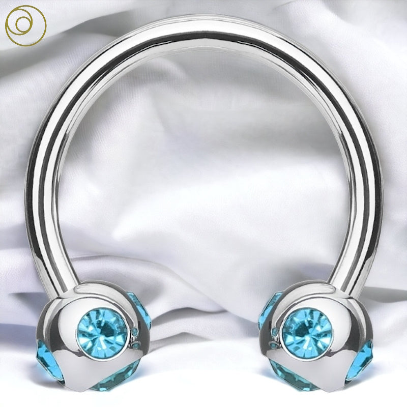 An aqua gem circular barbell with 5 gems on the balls of a surgical steel horseshoe barbell pictured against a white fabric background.