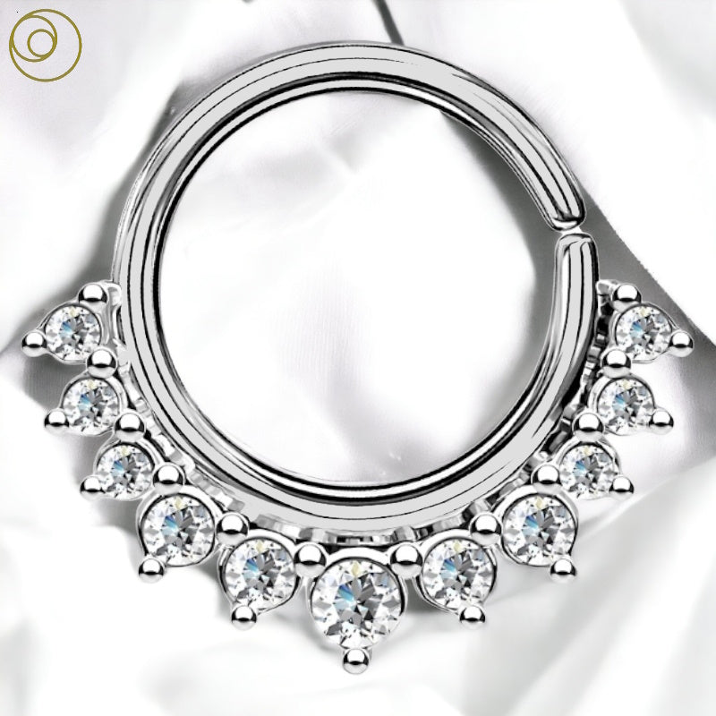 A surgical steel bendable crystal septum ring with paved crystals around the bottom half of the septum ring pictured against a white fabric background.