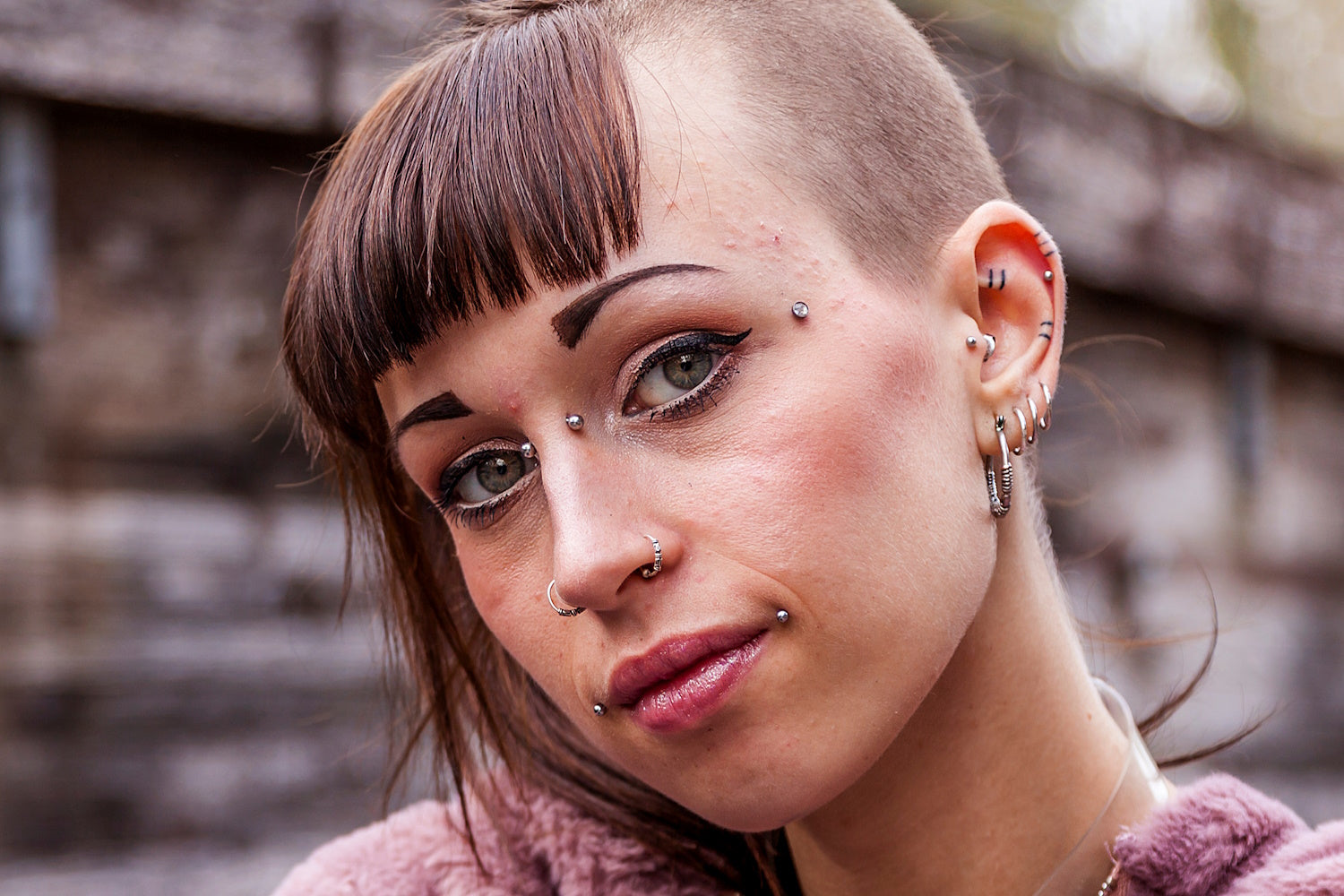 The face of a young woman with a bridge piercing along with many other piercings on her face and ears.
