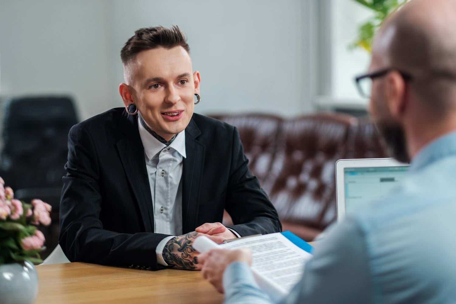 A man at a job interview that has large stretched earlobes and tattoos.