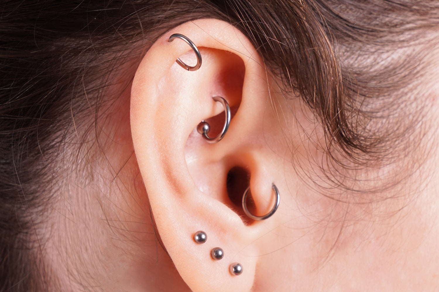 A rook, tragus, and helix piercing on the ear of a woman.