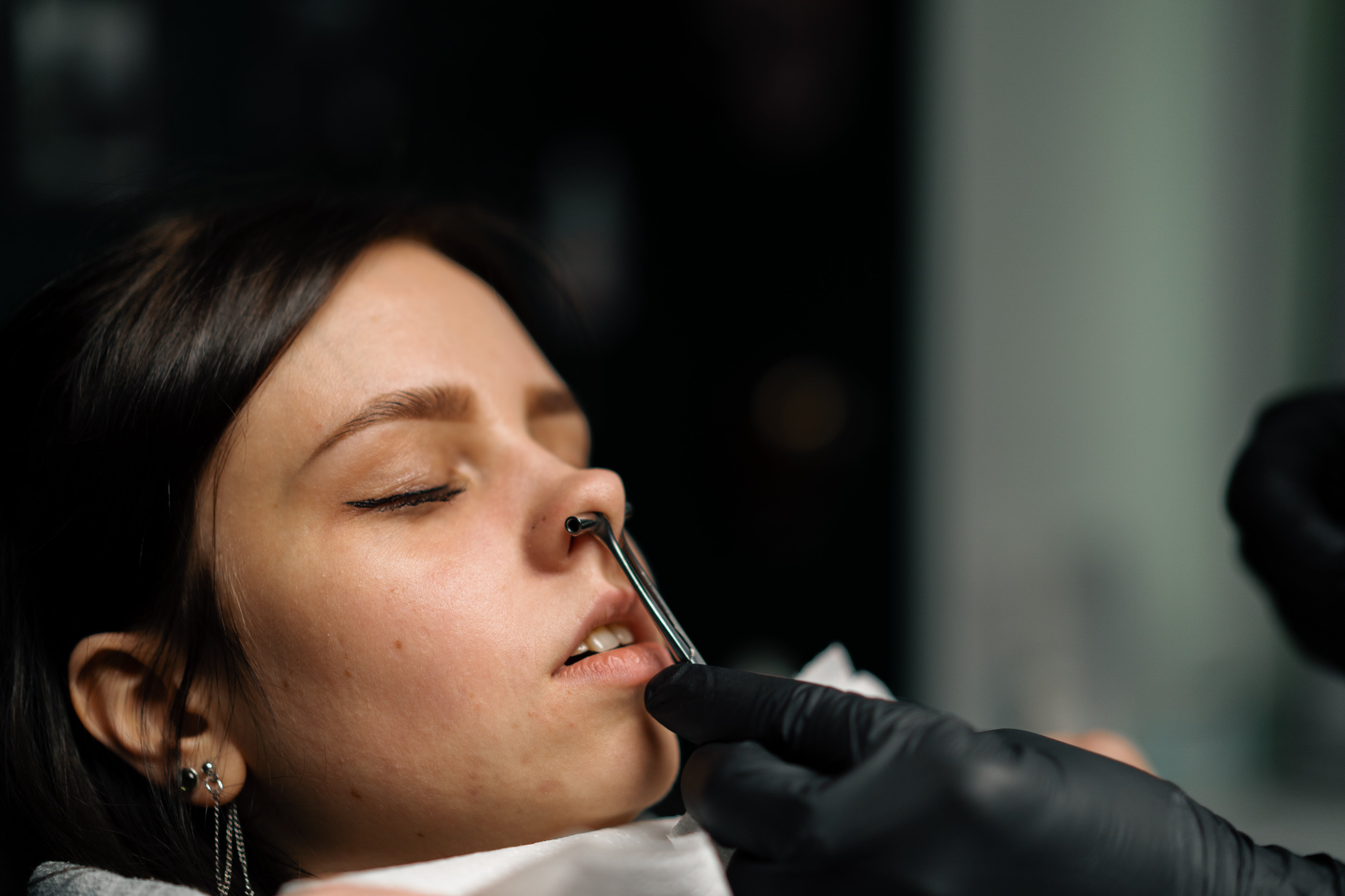 A woman getting her septum pierced shown with a hollow tube through the piercing.