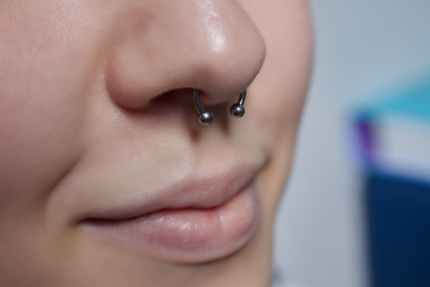 A close up of a septum piercing on a woman with a small circular barbell in it.
