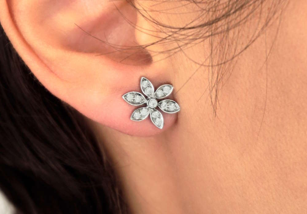 A woman with a single earlobe piercing with a flower design earring in it.