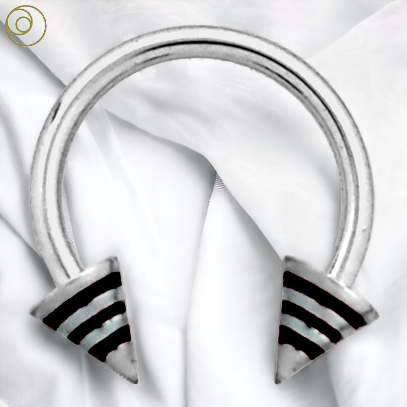 A surgical steel spiked horseshoe septum ring with black stripes on the spikes pictured against a white fabric background.