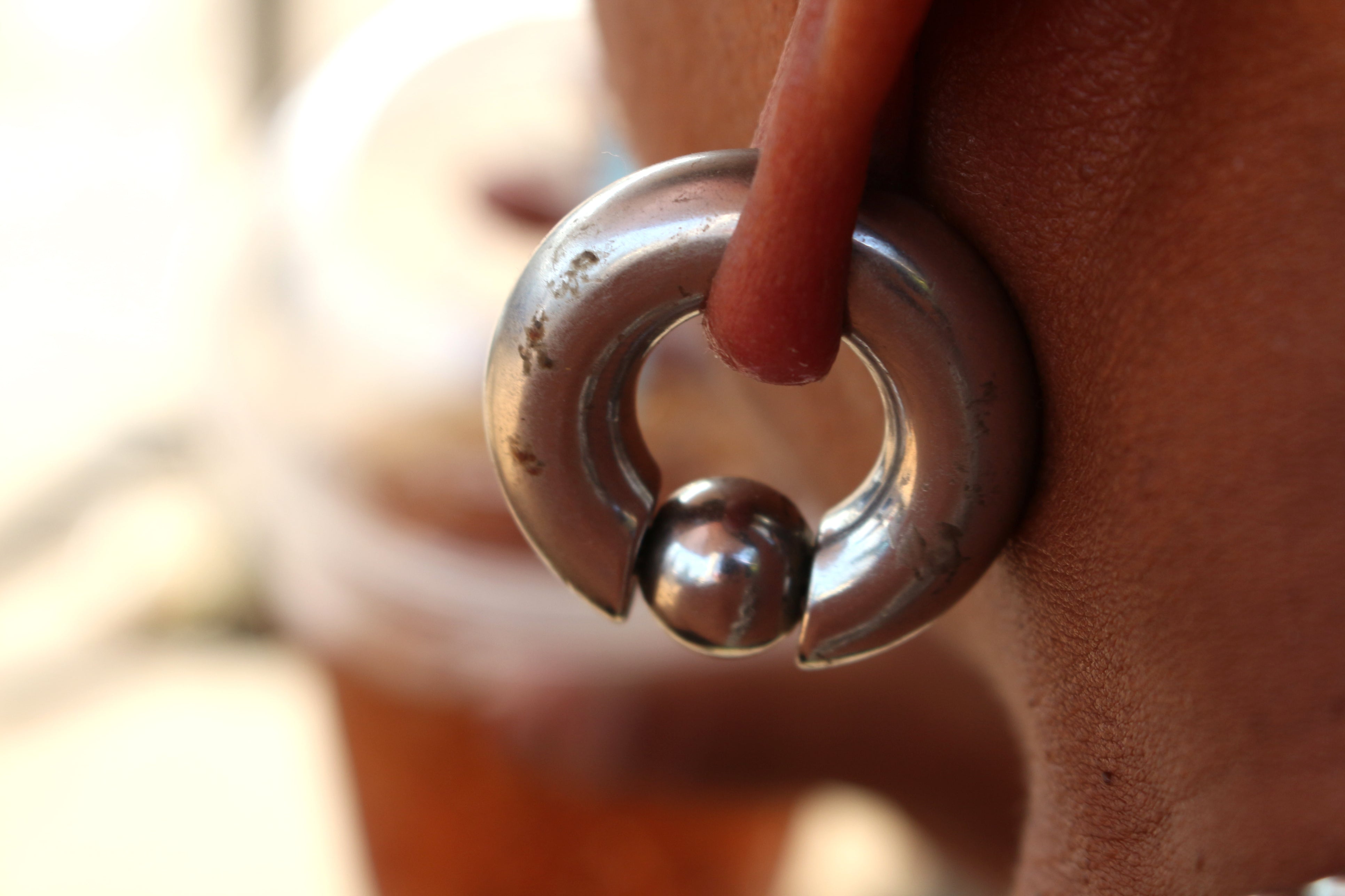 A man's stretched earlobe with a large gauge captive bead ring in it.