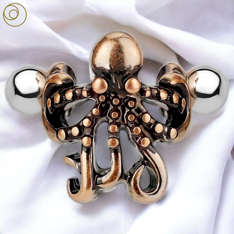 A surgical steel octopus ear cuff with a brass octopus on a barblell that fits in helix piercings pictured against a white fabric background.