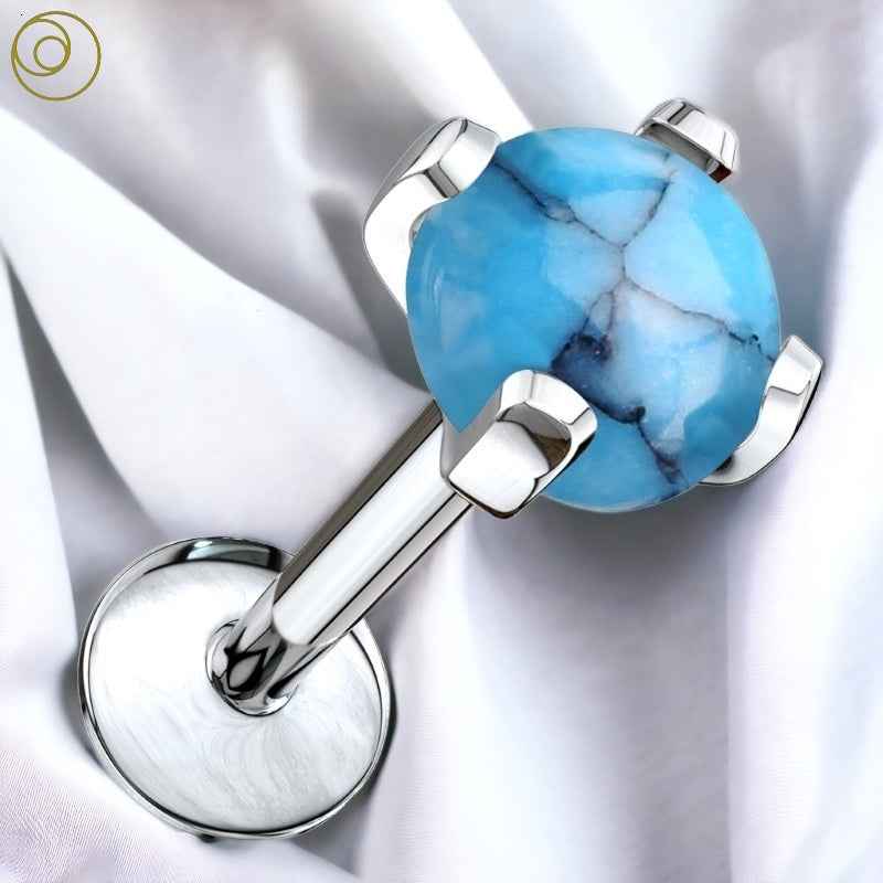 A turquoise stone labret stud with a surgical steel barbell pictured against a white fabric background.