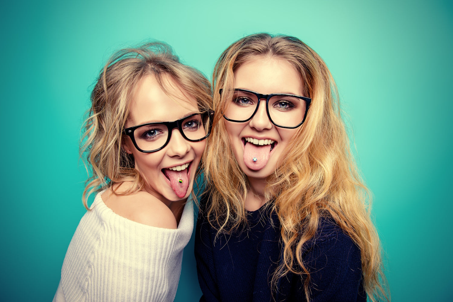 Two women each with their tongue sticking out showing their tongue piercings.