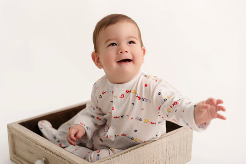 Happy baby boy in pima cotton pajamas, sitting and smiling in a wooden box