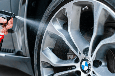 High-pressure cleaning of BMW alloy wheel with focus on water spray and logo.