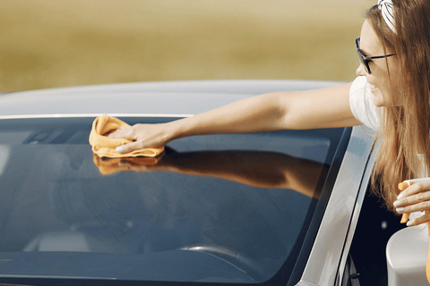 Female hands cleaning car exterior with a yellow rag, sunny day ambiance.