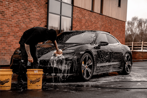 A person washing a black sports car in a parking lot.