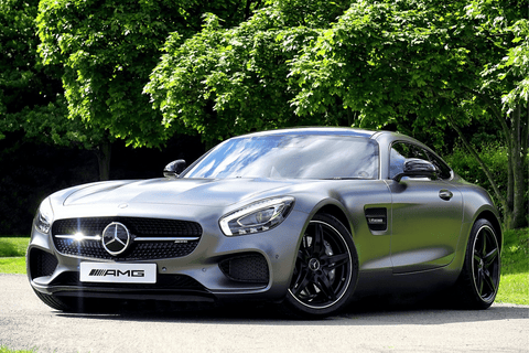 Matte gray Mercedes AMG GT sports car parked in front of lush green trees.