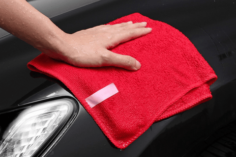 A person cleaning a car with a red towel.