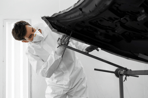 A person in a white suit is working on a car.