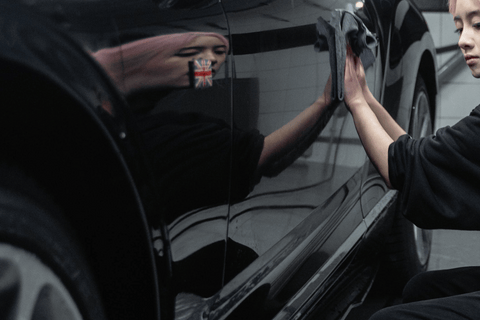 Detail of cleaning a car door with a microfiber cloth and visible flag reflection.