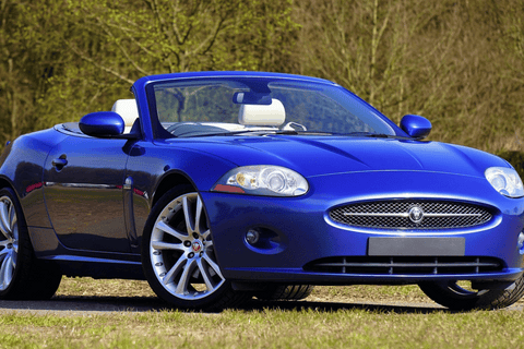 Blue Jaguar XK convertible sports car parked on a country road.