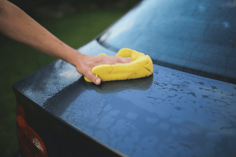 Close-up of a hand cleaning a wet car with a yellow microfiber rag.