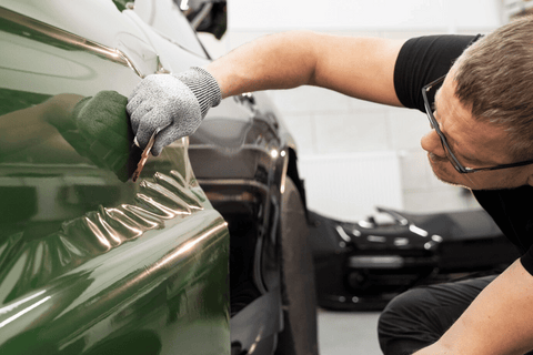 A person working on a green car in a garage.