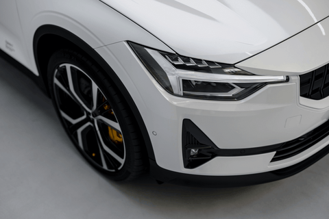 Close-up of a modern white car's angular headlight and sleek rim design.