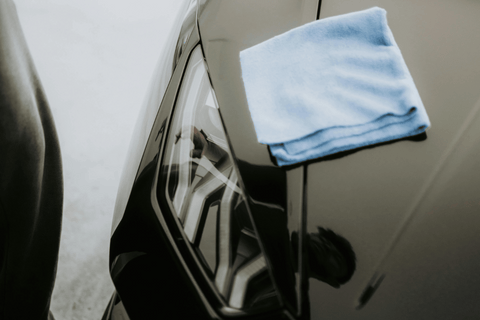 Close-up of a car detailing with a microfiber cloth on the glossy black surface.