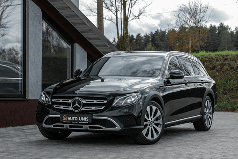 Black Mercedes-Benz parked outside modern building, overcast sky.