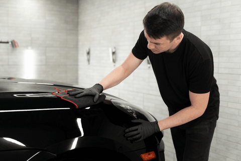A person in a black t-shirt and gloves is working on the hood of a black sports car.