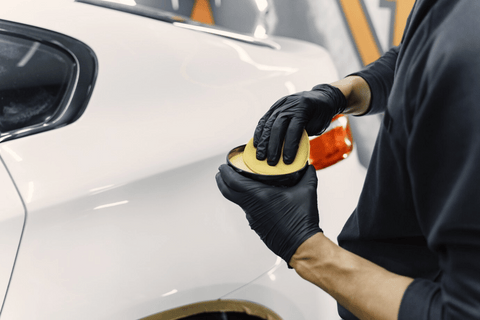 A person in black gloves polishing a white car.