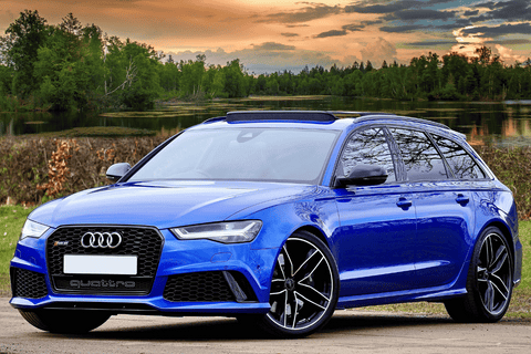 Blue Audi RS6 Quattro parked outdoors with scenic forest and sunset.