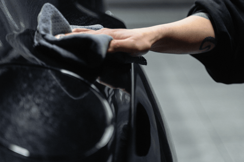 Detail of a black car being hand-washed with a dark rag.