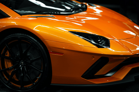 Bright orange sports car with sleek headlights and black wheels.