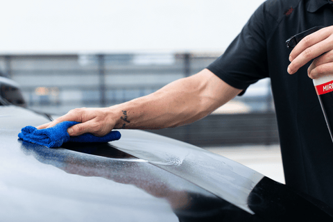 Detailing a car with a blue microfiber cloth and spray.