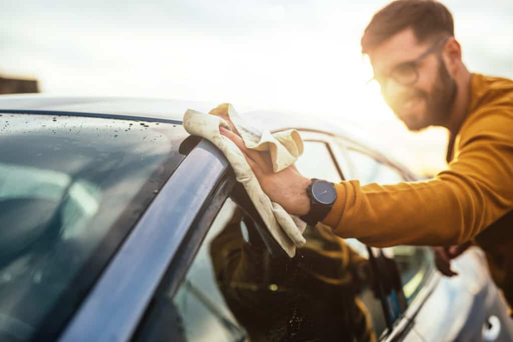 Shot of a happy young man cleaning his car with microfiber cloth on a sunny day.